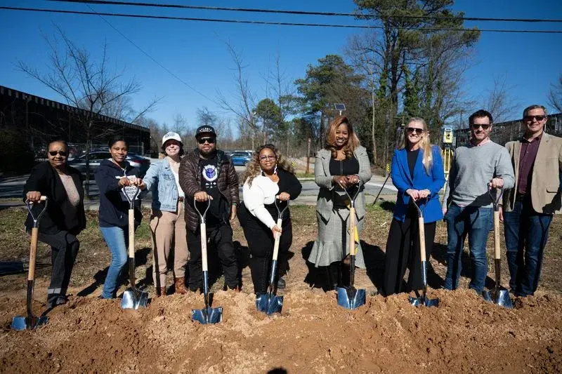 A group of people breaking ground with shovels in dirt outside.