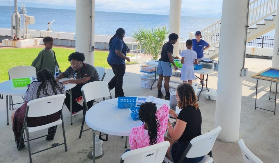 Children and adults around white round tables working on activities at the New Canal Lighthouse Museum and Education Center