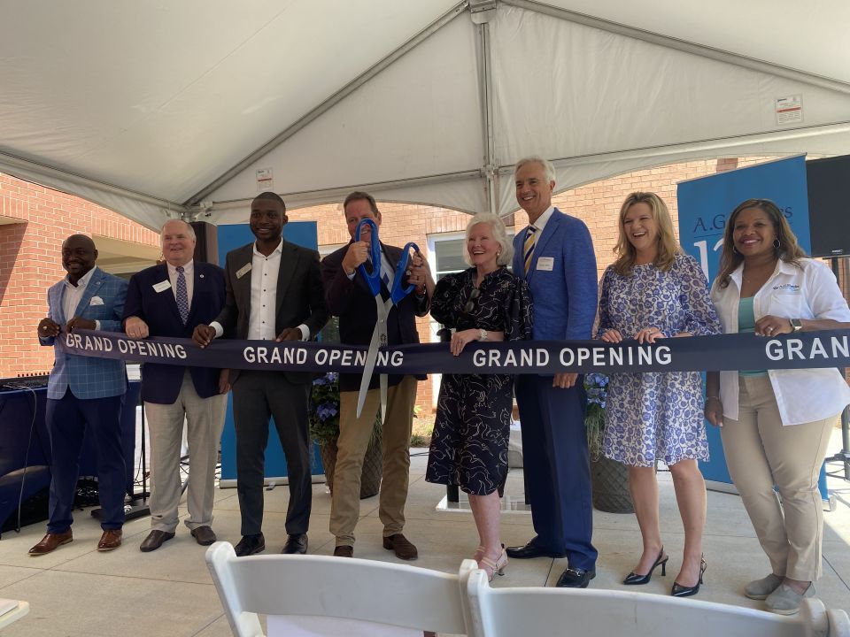 Officials in professional attire cut a grand opening ribbon in front of a new development
