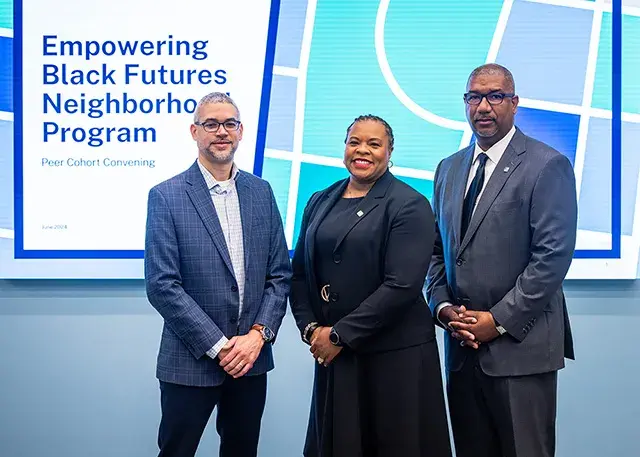 The people in blue, black and gray suites standing in front of a screen