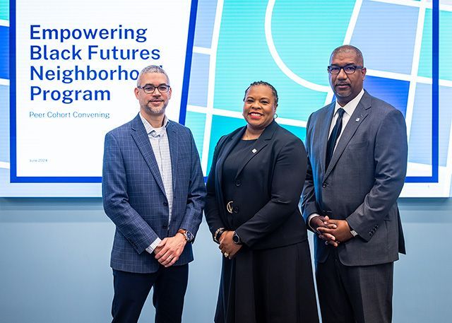 The people in blue, black and gray suites standing in front of a screen