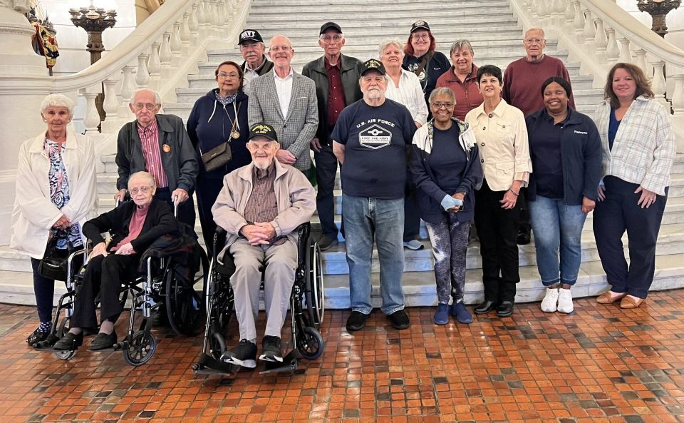 A group of people, including two people in wheelchairs, stand at a grand staircase