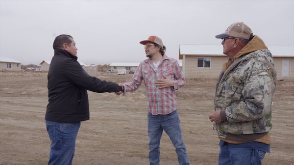 Two men shaking hands while third man looks on