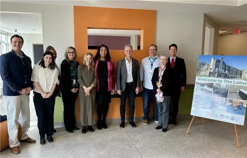 Group of people stand together smiling with a sign on the right that reads, "The Lotus."