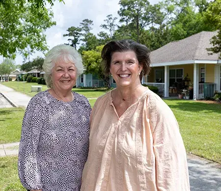 Two women stand in front of homes on a neighborhood block