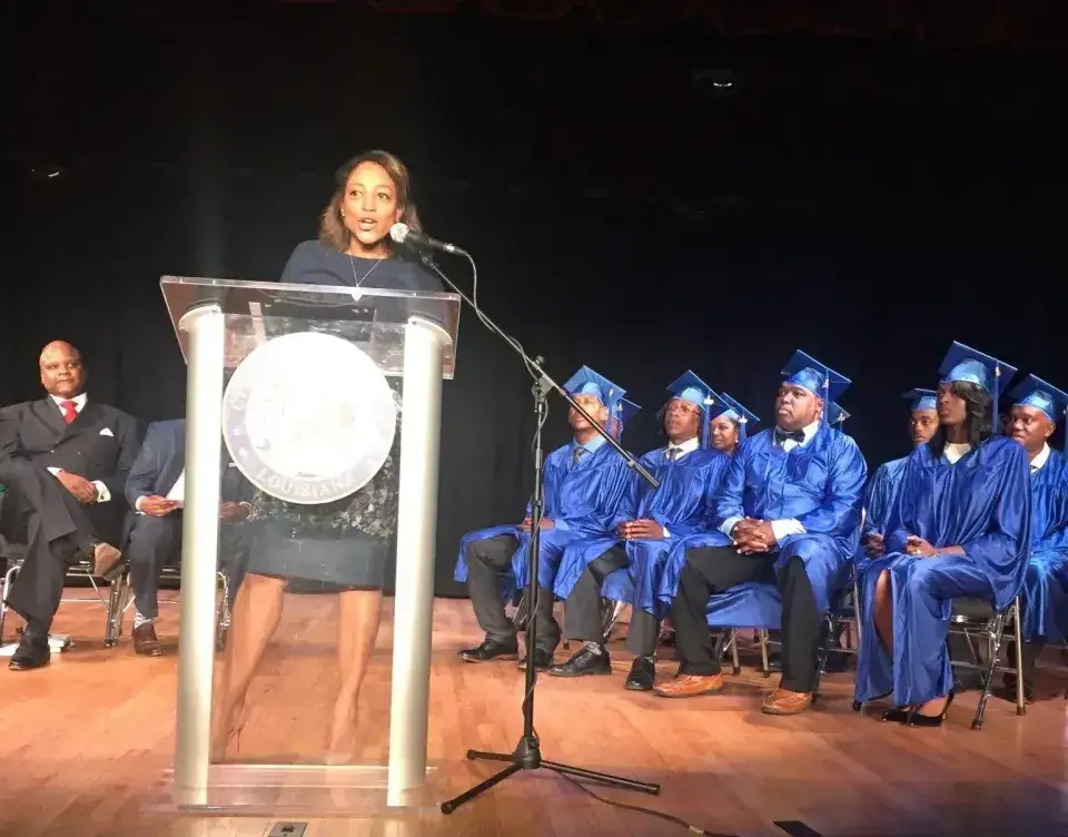 Rachelle Delfillo speaks from a podium to graduating students wearing blue cap and gowns