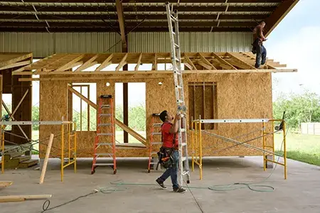 A man carries a tall ladder as he walks in front of a home under construction