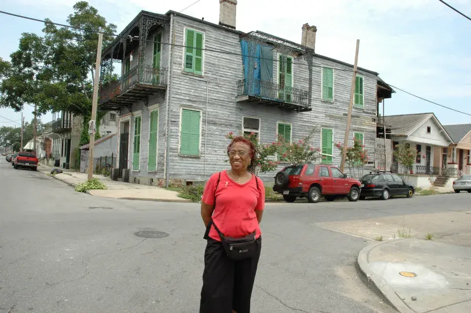 Emelda Paul in front of a building damaged by Hurricane Katrina