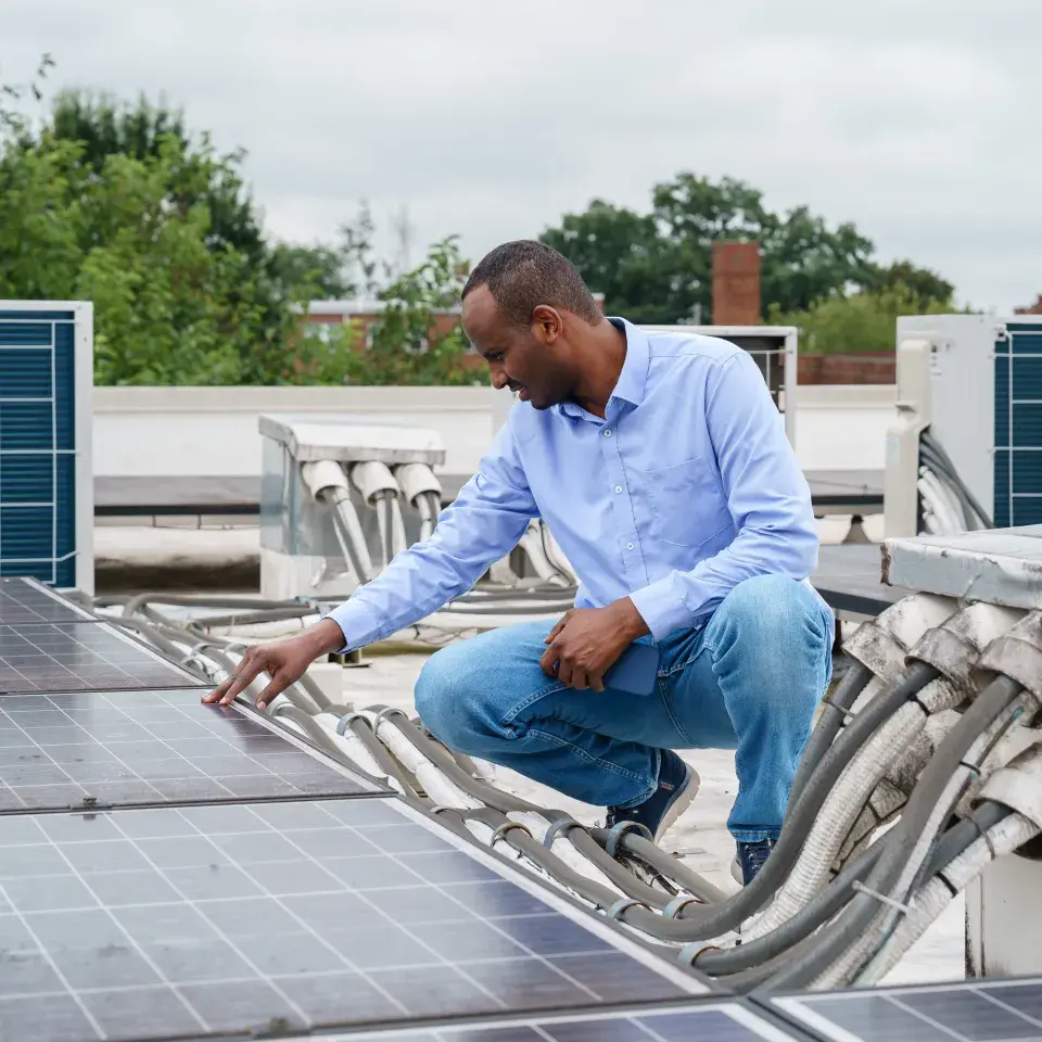 Person in blue dress shirt and jeans examines rooftop solar array