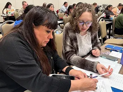 Participants at the California Tribal Housing Accelerator Academy in discussion while they review documents at their desks