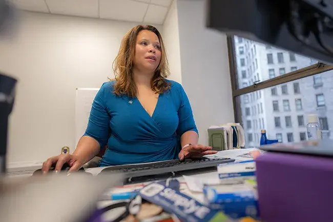 A woman in a teal blouse sitting at a desk working on the computer