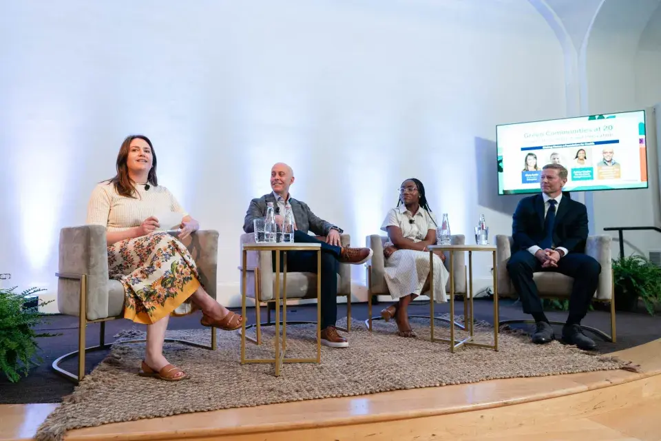 Four people seated on stage in semi-circle of beige velvet chairs 