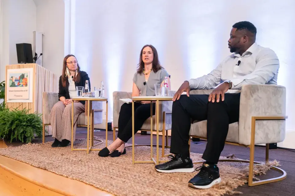 Three people seated on stage in beige velvet chairs arranged in semi-circle