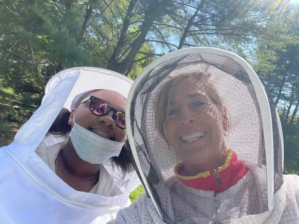 Two people stand smiling next to each other wearing beekeeping attire