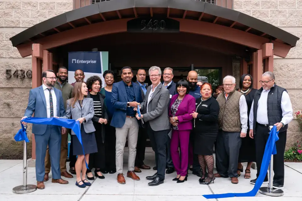 Group of people stand smiling in front of a building's entrance after just cutting a long blue ribbon