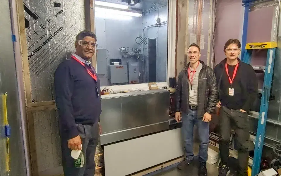 Three people stand in front of a mechanical structure