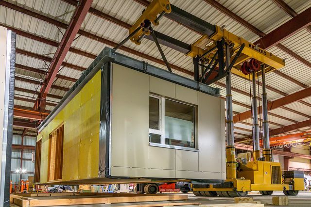 A room being built inside a warehouse and lifted by a specialized lifting equipment