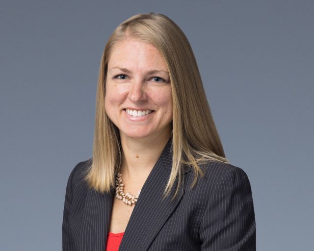 Woman with shoulder-length blond hair wearing a red blouse and a black jacket