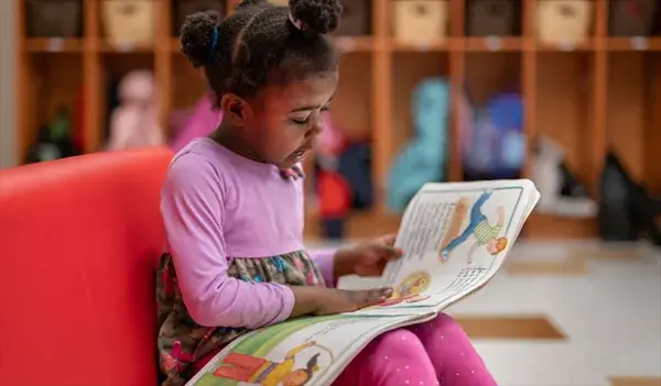 Little girl in pink and floral dress reading a picture book