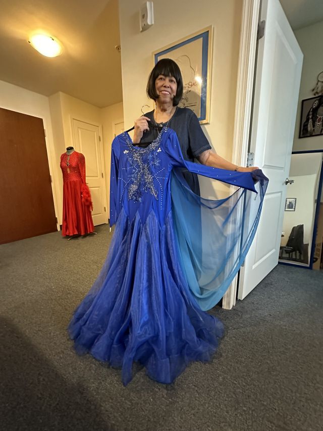 Person stands smiling and displaying a blue ball gown