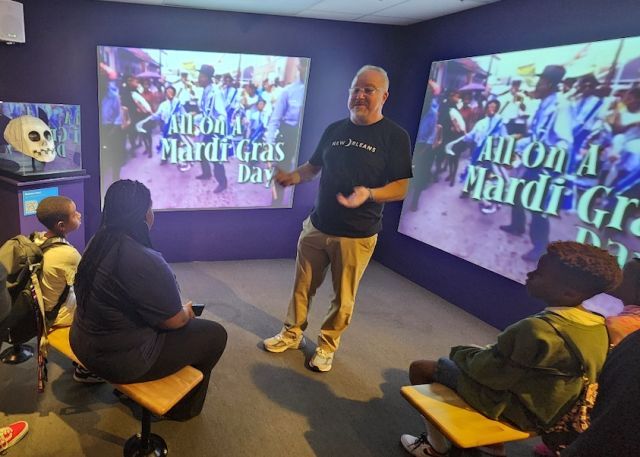 Man standing in front of room teaching children about New Orleans cultural history