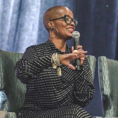 Black woman wearing glasses and white-black polka dot dress speaking with a mic