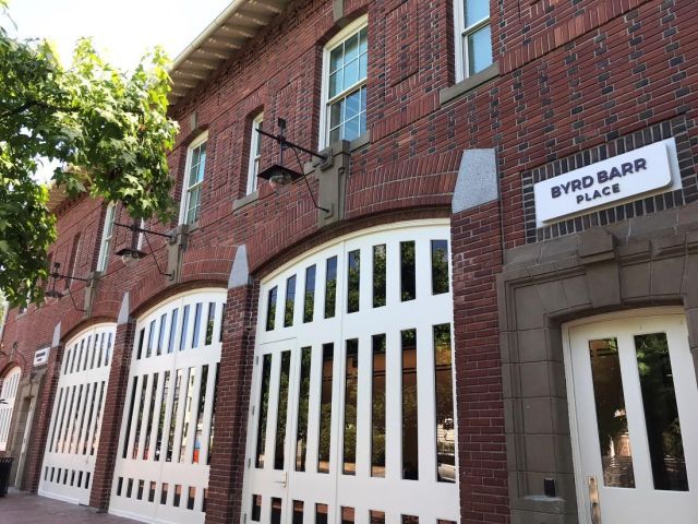 Exterior of brick building with three garage doors and the name "Byrd Barr Place" over the front entrance, a white door with two glass panes