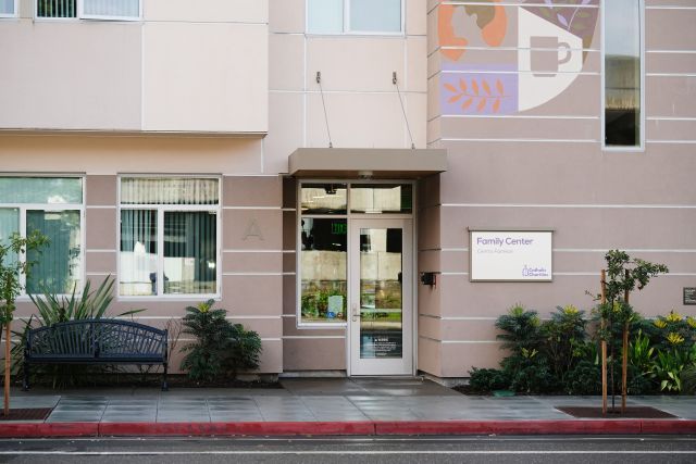 Sand-colored building exterior featuring a glass front door and a sign that reads "Family Center" and "Centro Families" with the Catholic Charities logo