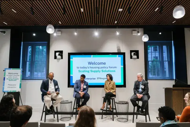 Four people sitting on stools conversing with an audience in front of them