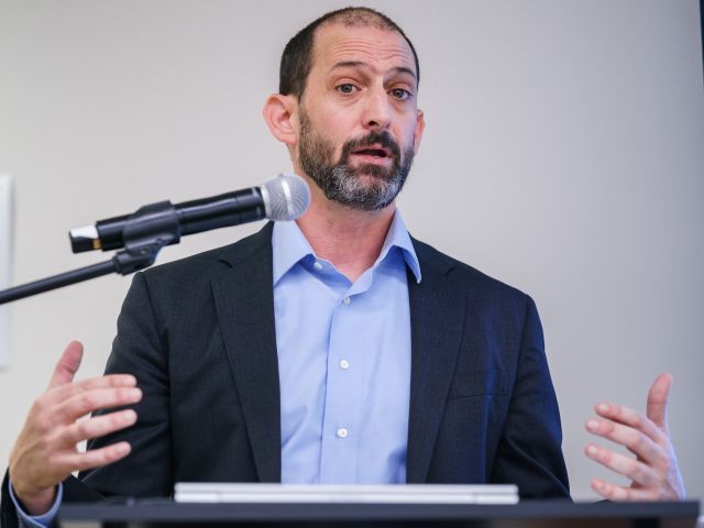 Person stands at podium speaking into mic gesturing with his hands