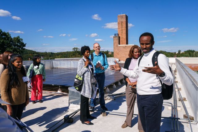 Group of people stand talking on a rooftop with solar panels in the background