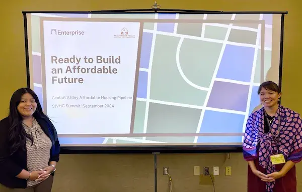 Two smiling women standing in front of screen with a Ready to Build an Affordable Future slide