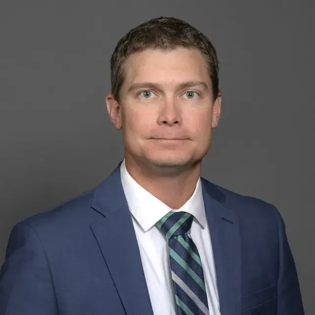 Person with short hair wearing a dark jacket, white dress shirt and striped tie