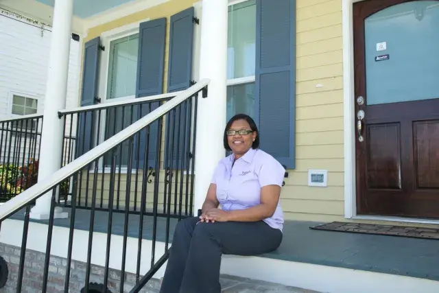 Smiling woman sitting on the steps of a yellow home.