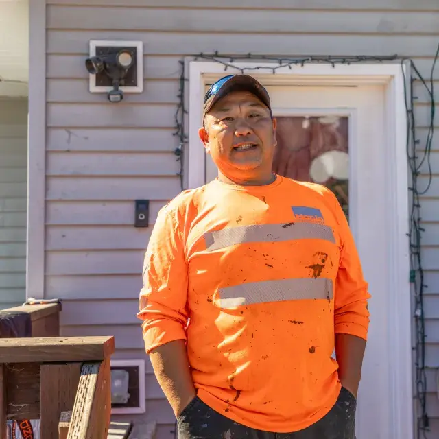 Person wearing bright orange shirt and cap stands in front of a house