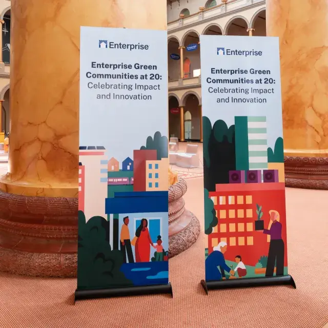 Two vertical signs in front of large columns read: Enterprise Green Communities at 20