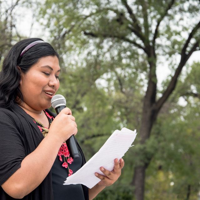 woman standing outdoors talking into a microphone