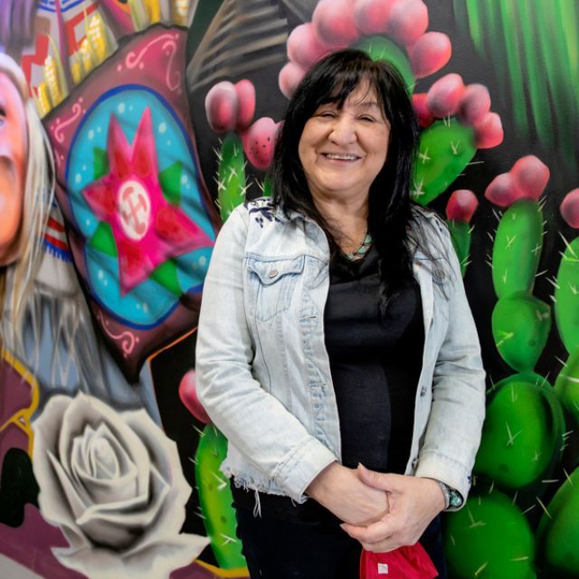 A woman posing up against a wall where a colorful mural is painted