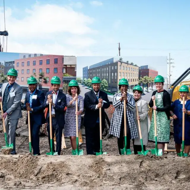 A group of people lined up with green shovels and hard hats for a groundbreaking
