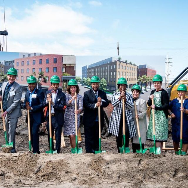 A group of people lined up with green shovels and hard hats for a groundbreaking