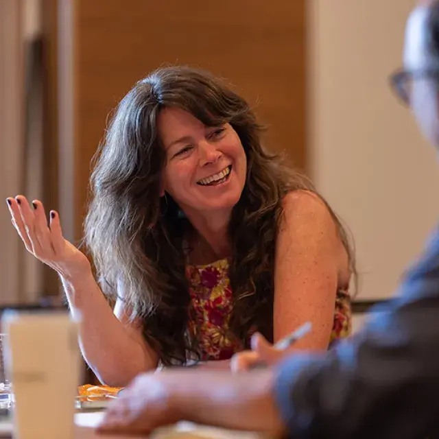 A woman and man sitting at a table talking as the woman smiles and gestures with her hands