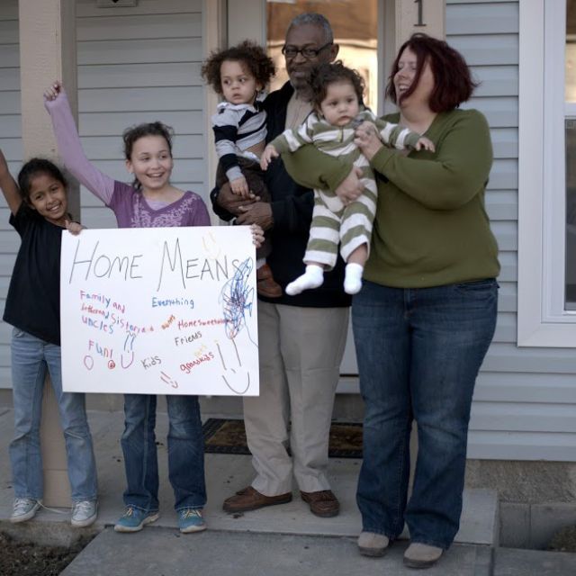 A family standing outside of their home with a sign