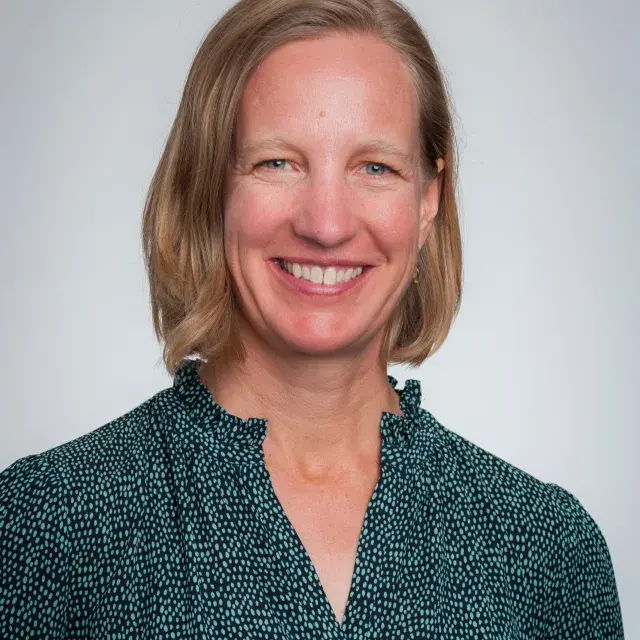 Person smiling with light brown hair and black patterned blouse.
