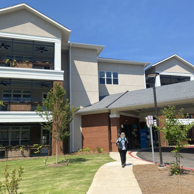 A woman entering the new development with a covered roundabout driveway and state of the art new homes with lush balconies.