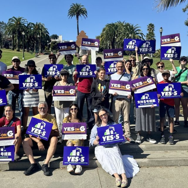 A group of people holding blue, Yes on Prop 5 signs in front of a park setting