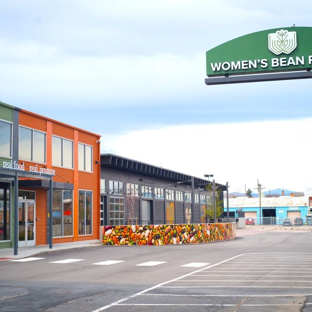 Green and orange 2-story building with a sign on the right that reads, Women's Bean Project