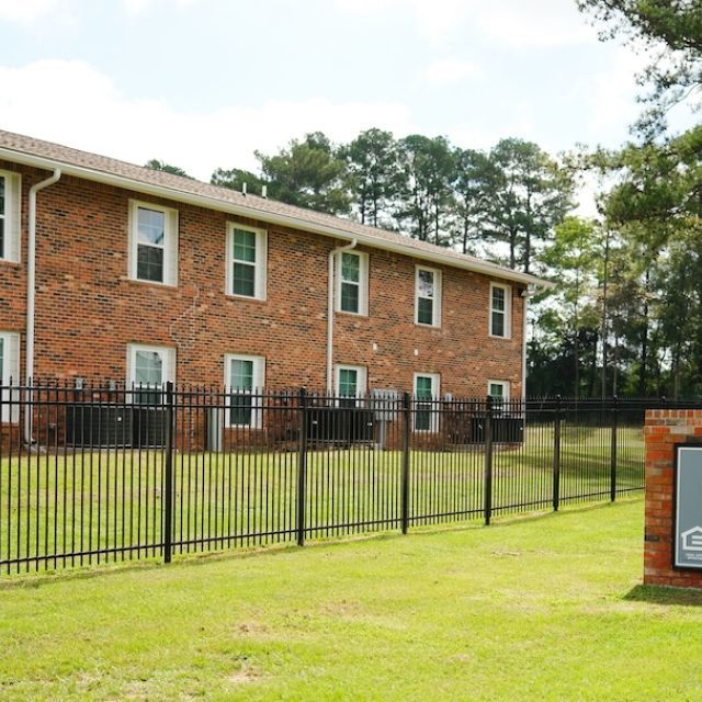 Red-brick apartment building, black fence and green lawn