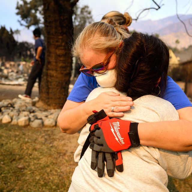 Two women hugging in their neighborhood devastated by wildfires