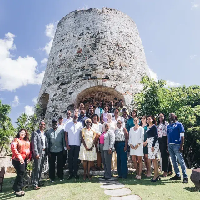 Attendees at the Housing Our Community Workshop in St. Croix, USVI stand in front of a historic structure with trees beside it