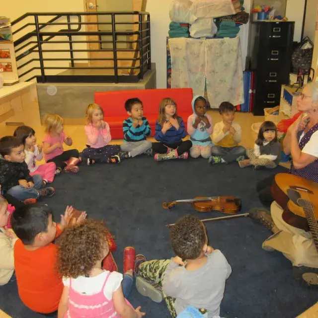 Children sitting on the floor in a circle participating in a music lesson